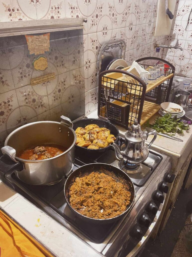 Une cuisinière avec deux casseroles de nourriture, représentant un Repas chez l'habitant à Marrakech.
