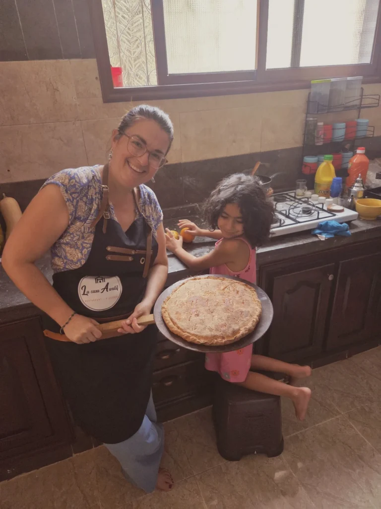 Fin du cours de cuisine à Ouarzazate : l'invitée, souriante, présente la pizza du désert sortie du four, avec Sofia.