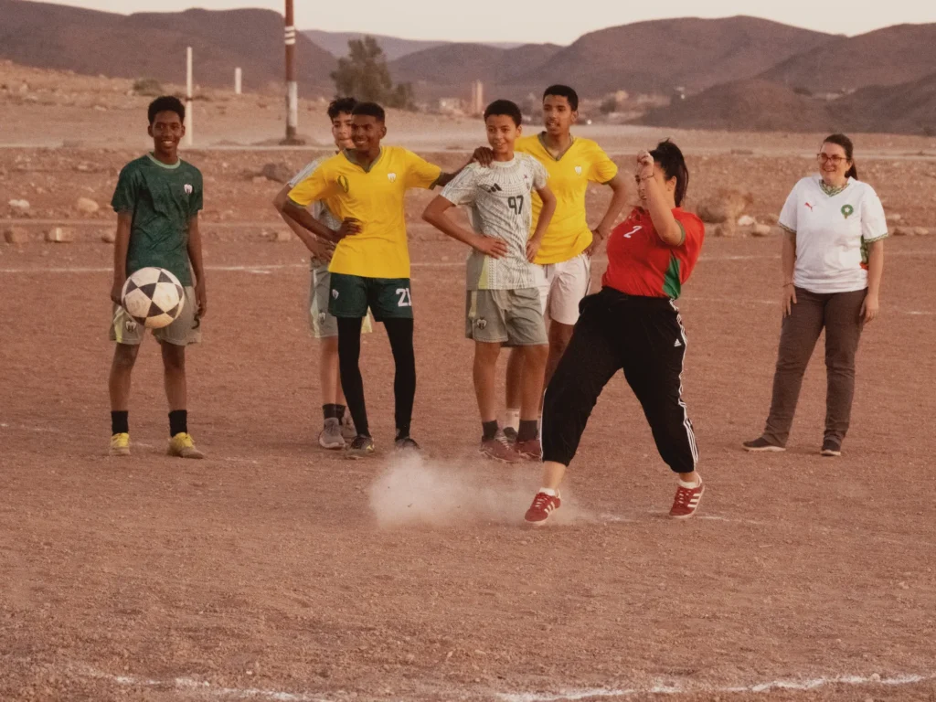 Une voyageuse frappe le ballon sous le regard amusé des jeunes, pendant le foot avec les locaux à Ouarzazate.