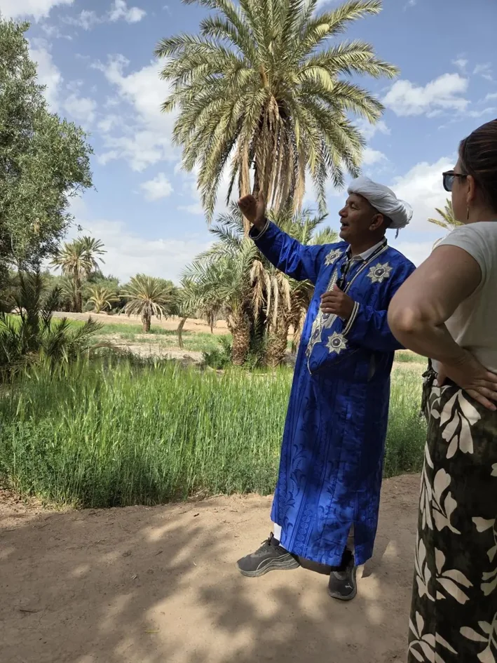 Guide local en djellaba bleue expliquant la palmeraie de Skoura à une voyageuse
