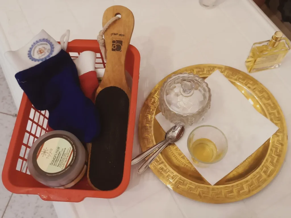 Hammam traditionnel à Ouarzazate : le panier du hammam avec gant kessa, savon noir et brosse, et un plateau d'huile parfumée