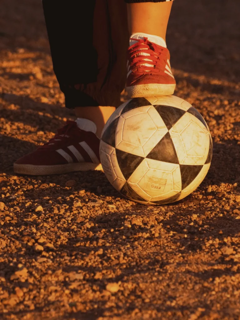 Pied en baskets posé sur un vieux ballon, sur le terrain en terre du match de foot à Ouarzazate.