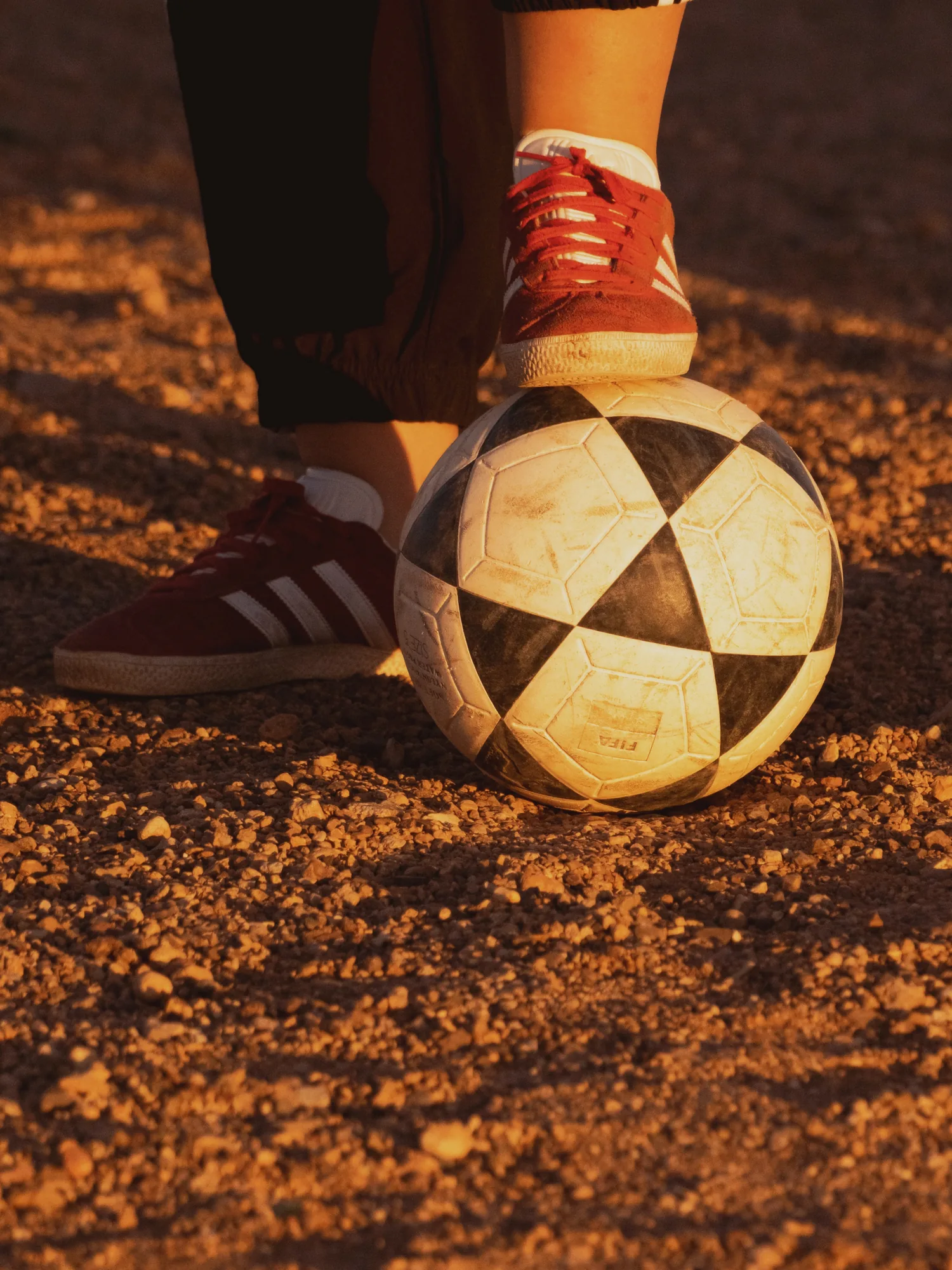 Pied en baskets posé sur un vieux ballon, sur le terrain en terre du match de foot à Ouarzazate.