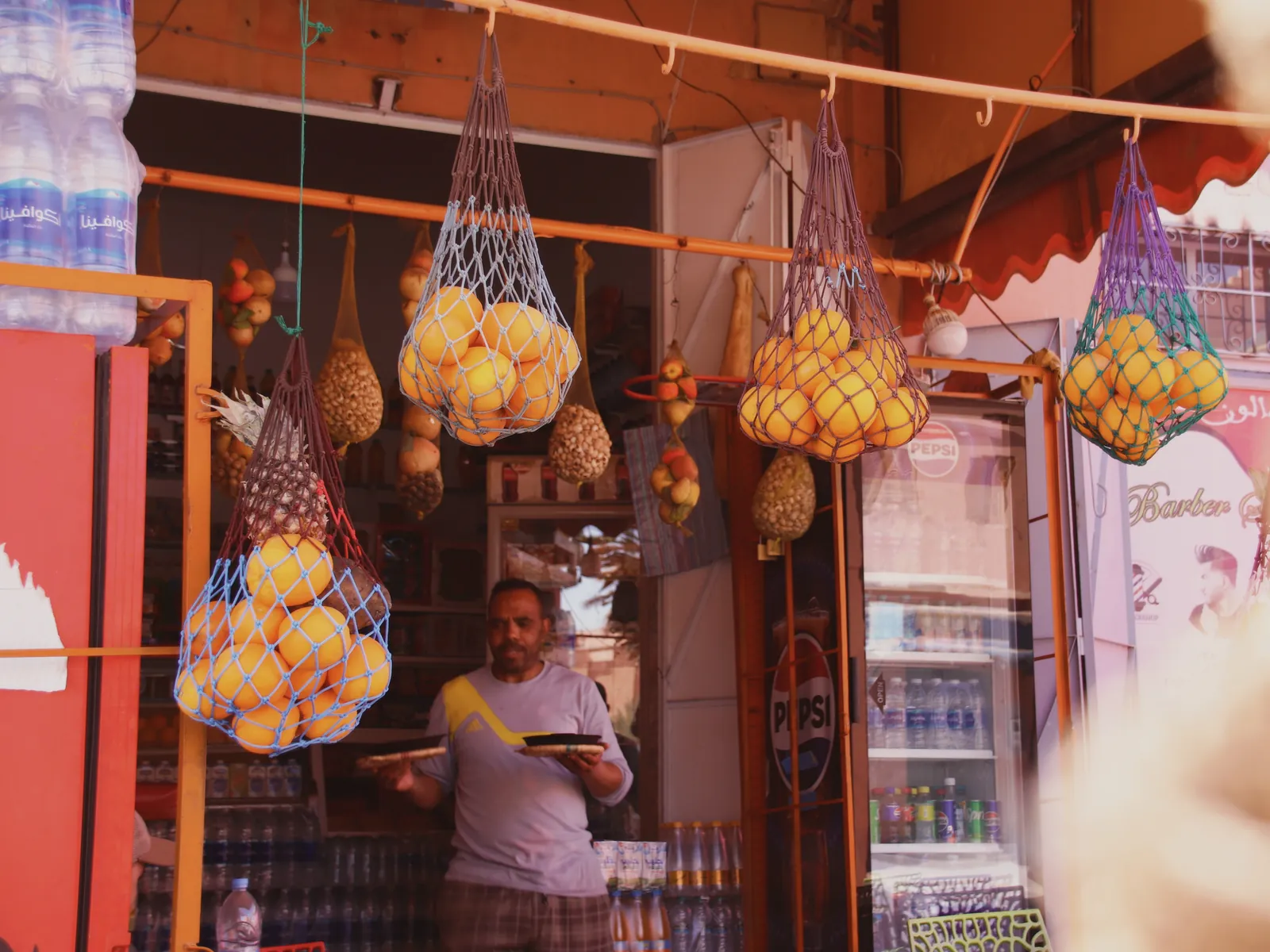 Photo tour à Ouarzazate insolite : une épicerie du centre-ville aux filets d'oranges suspendus, son gérant à l'intérieur