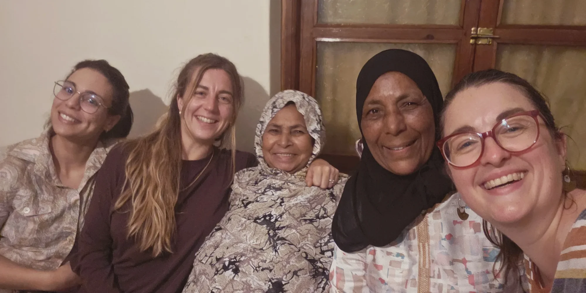 Repas chez l’habitant à Ouarzazate : deux hôtesses et trois voyageuses rient ensemble sur le canapé du salon familial.