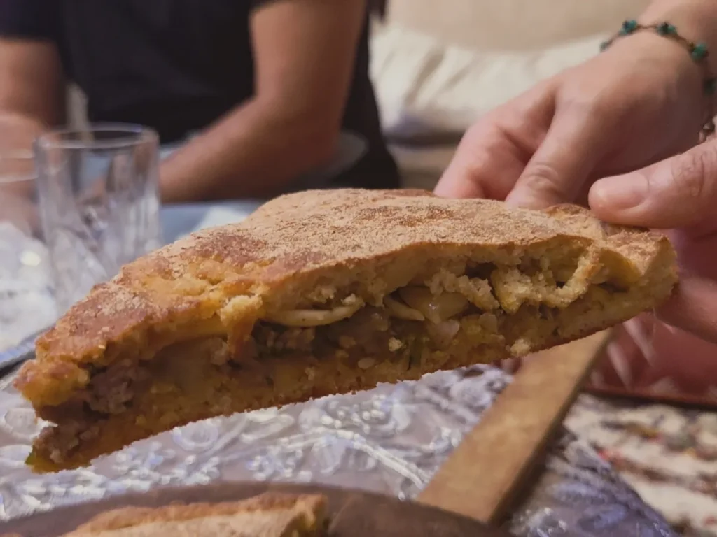 Repas chez l'habitant à Ouarzazate : une part de pizza medfouna farcie à la viande et aux oignons, servie à table